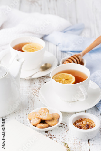 Two cups of hot black tea, lemon, homemade cookies and honey on white rustic wooden background. Breakfast concept.