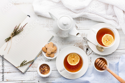 Two cups of hot black tea, lemon, homemade cookies and honey on white rustic wooden background. Breakfast concept. Top view, flat lay style