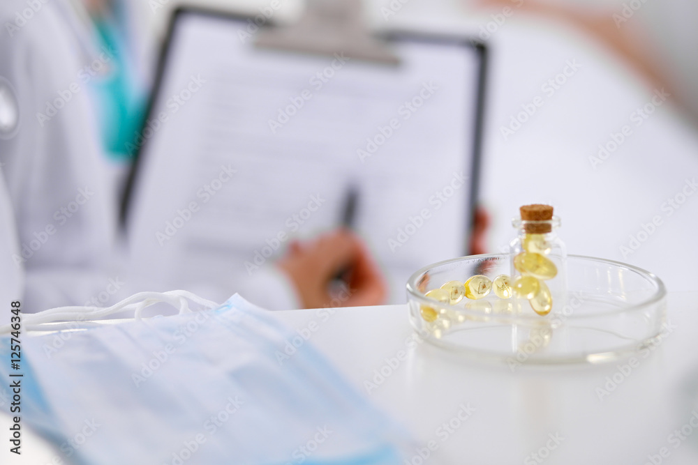 Medicine capsules and pills are lying against the background of a doctor writing prescription. Patient is in the bed and ready to take medication. Medicine capsules and pills are lying against the background of a doctor writing prescription. Patient is in the bed and ready to take medication.