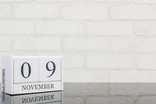 Closeup white wooden calendar with black 9 november word on black glass table and white brick wall textured background with copy space , selective focus at the calendar