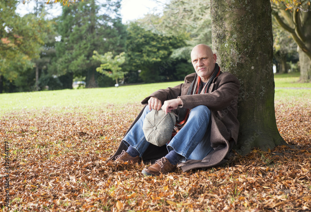 Portrait of a happy mature man sitting under a tree in autumn 