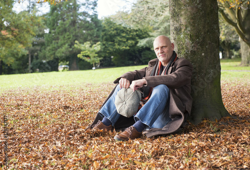 Portrait of a happy mature man sitting under a tree in autumn 