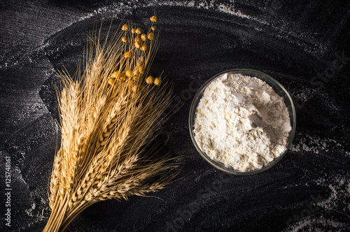 Flour in a glass bowl and wheat ears. On a black background.Top view. Flat lay.