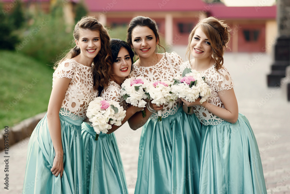 Naklejka premium Bridesmaids in white lace blouses lean to each other standing ou