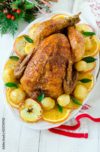 Christmas baked chicken (turkey) with oranges and apples on a wh