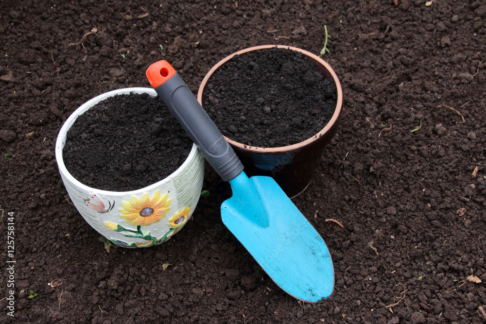 Ceramic flowerpots filled with the fresh soil for planting and a garden trowel in the polycarbonate greenhouse prepared for wintering Ceramic flowerpots filled with the fresh soil for planting and a garden trowel in the polycarbonate greenhouse prepared for wintering