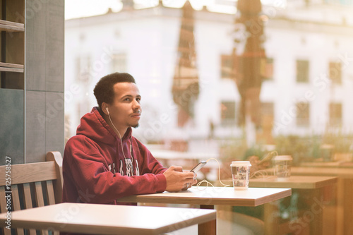 young african man sitting at a cafe and listening music from his mobile phone