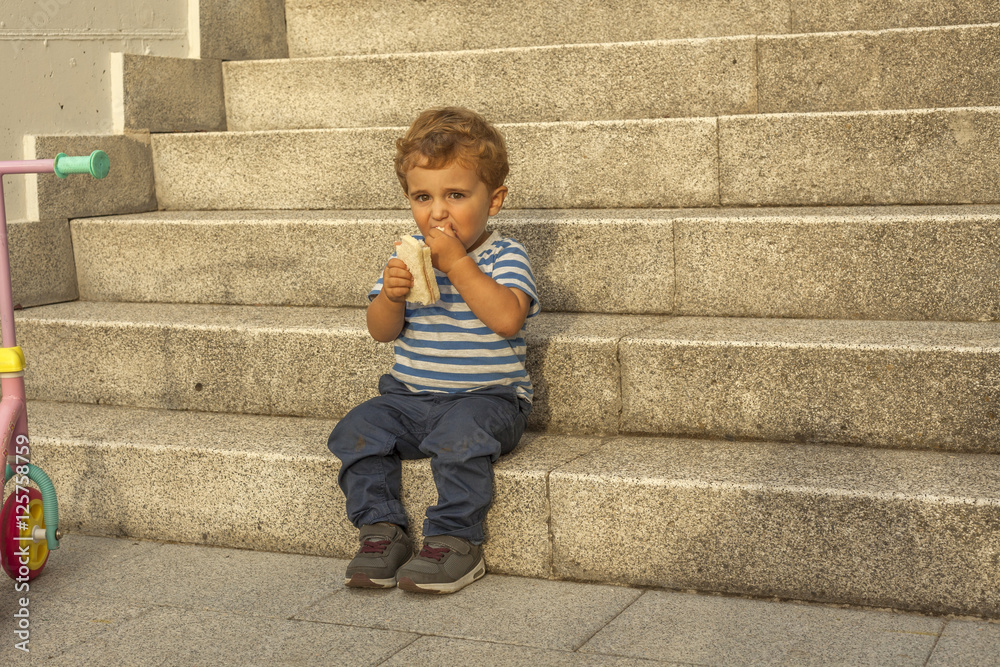 Full shot portrait cute baby boy having a snack sit in stone sta Full shot portrait cute baby boy having a snack sit in stone sta