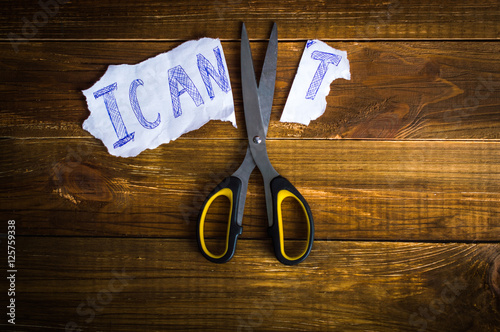 Scissors cut the inscription "I can't" on paper. On a wooden background.Top view. Flat lay.