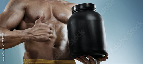 Sport backgrounds. Strong bodybuilder holding a plastic jar with a dry protein and showing gesture. Isolated. Sport food