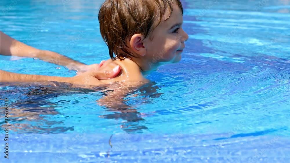 Little boy swimming in a pool, his dad helping him Little boy swimming in a pool, his dad helping him