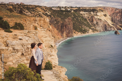 Romantic and stylish caucasian couple standing on the background of spectacular sea view. Love, relationships, romance, happiness concept. © anna_gorbenko