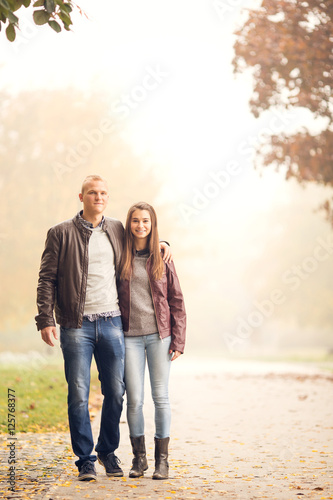 Young couple are walking in a park on a one Autumn day. They are hugging and smiling and enjoy being together