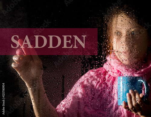 sadden written on virtual screen. young woman melancholy and sad at the window in the rain, she holding a cup of hot coffee or tea