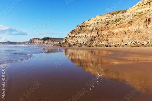 Mountain reflected in the smooth water of the beach Areia Branca. Lourinha, West coast of Portugal