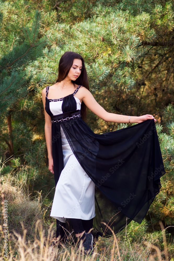 Graceful charming brunette model posing in black dress in coniferous park Graceful charming brunette model posing in black dress in coniferous park