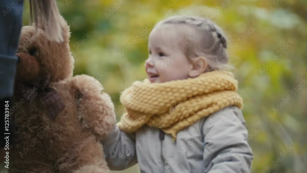 Joyful little blonde girl plays with teddy bear in autumn park