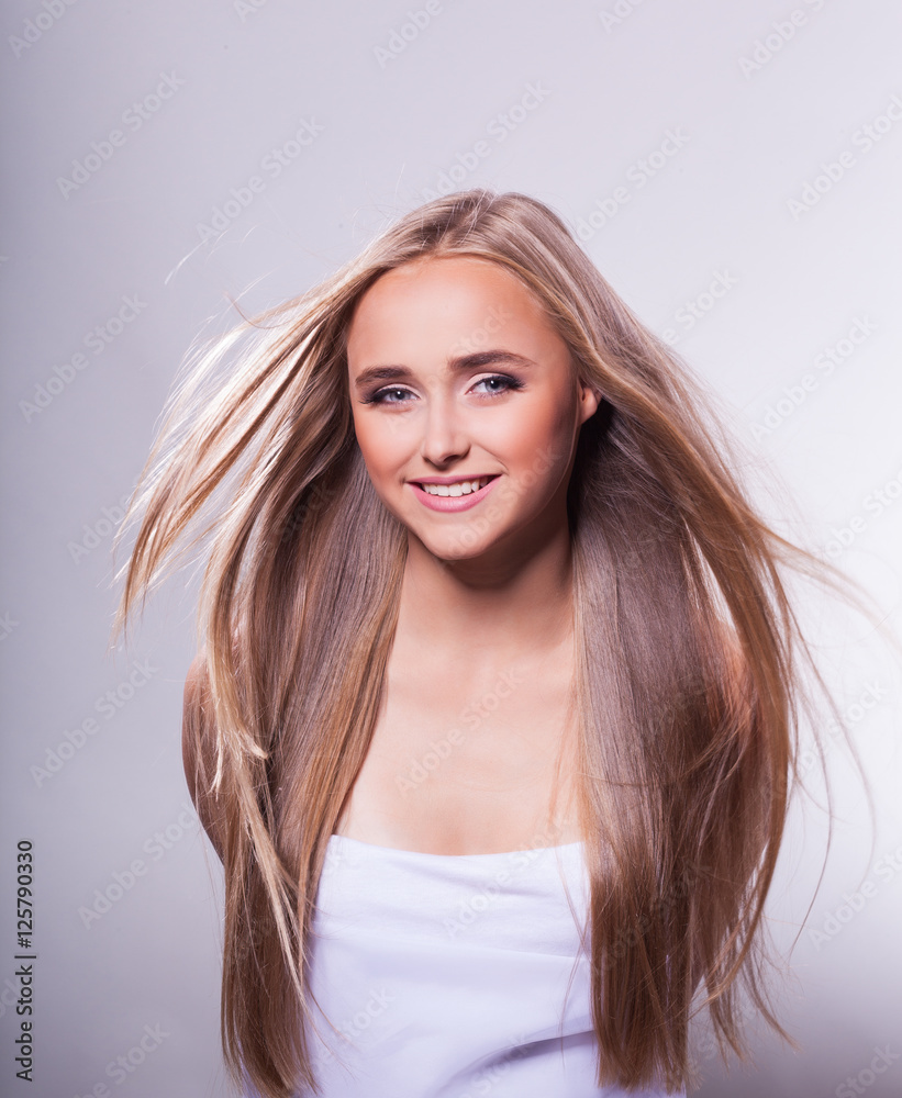 Fototapeta premium Beautiful young girl with long hair on a light background in the studio