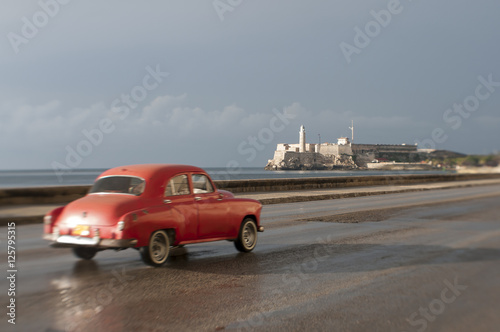 Dreamy tilt-shift scenic view of vintage American car taxi driving in front of el Morro lighthouse along the Malecon in Central Havana, Cuba © lazyllama