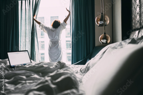 Woman stands near the window in hotel room at morning time photo