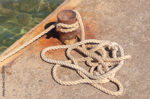 Rusty bollard with bounded mooring at sea pier photo