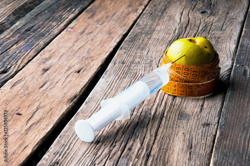 Green apple wrapped with tape measure being injected with syringe