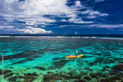 Female and little boy paddling canoe on a lagoon with coral reef