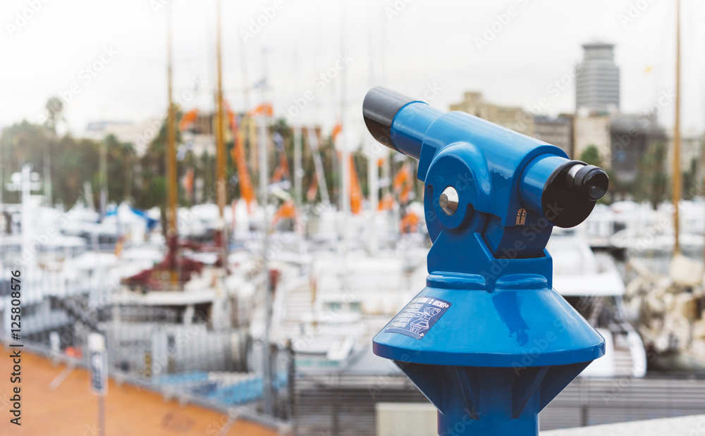 Touristic telescope look at the city with view of Barcelona Spain, close up old blue binoculars on background viewpoint  the pier port yacht, coin operated  in panorama observation nature, mockup