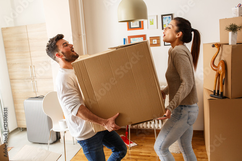 Young married couple carrying big cardboard box into new home. Moving house.	 photo