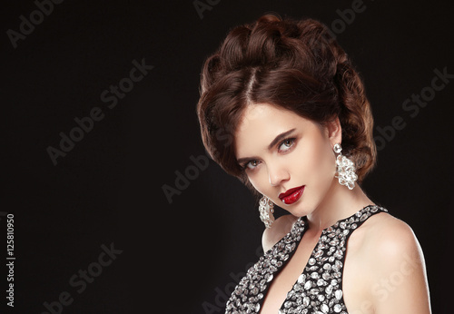 Fashion jewelry. Woman beauty portrait. Elegant Hairstyle. Red lips makeup. Attractive brunette in luxury beaded black dress isolated on black background.