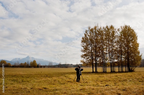 Photographer using a professional digital camera on a tripod   natural landscape on background