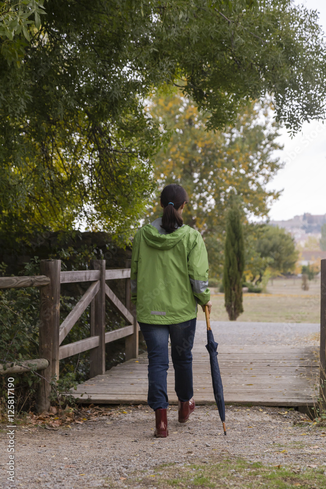 Woman walking with an umbrella in a park with yellow leaves falling from trees Woman walking with an umbrella in a park with yellow leaves falling from trees