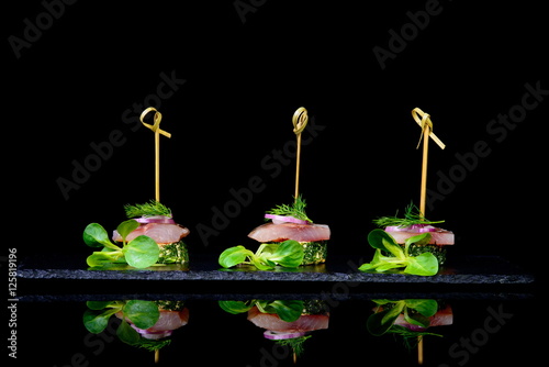 canape with herring and onion on black background