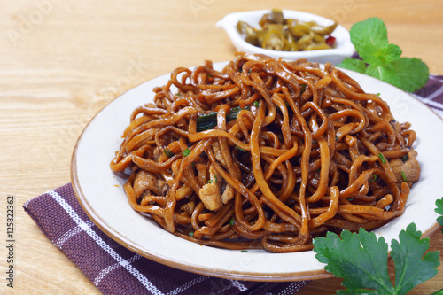 yi mein noodle stir fried with dark caramel sauce on wooden table, served together with a small plate of sour taste green chili, makes a delectable authentic malaysian chinese street food.