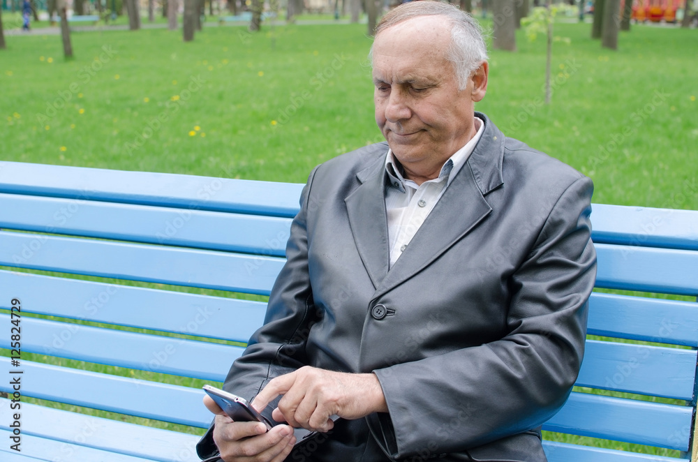 Fototapeta premium Aged man is using cellphone in the park