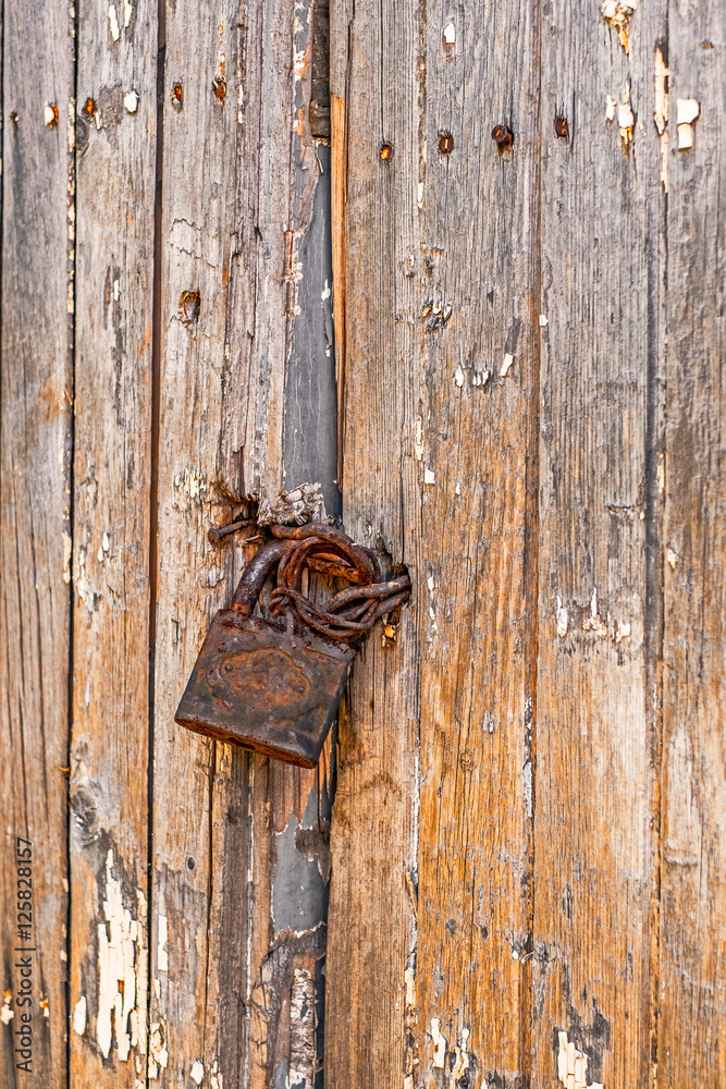 Old weathered grunge rusty locked padlock on old wooden board door, vertical view Old weathered grunge rusty locked padlock on old wooden board door, vertical view
