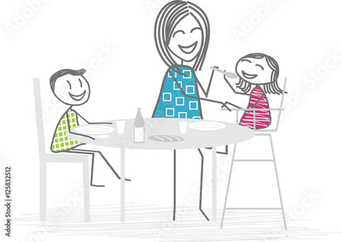 Une mère ou nounou fait manger un jeune enfant autour d'une table, un deuxième enfant mange seul photo