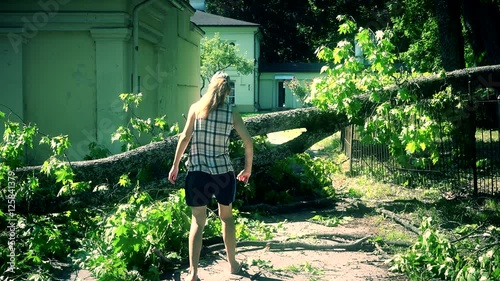Worried woman climbing over fallen tree on house yard entrance.