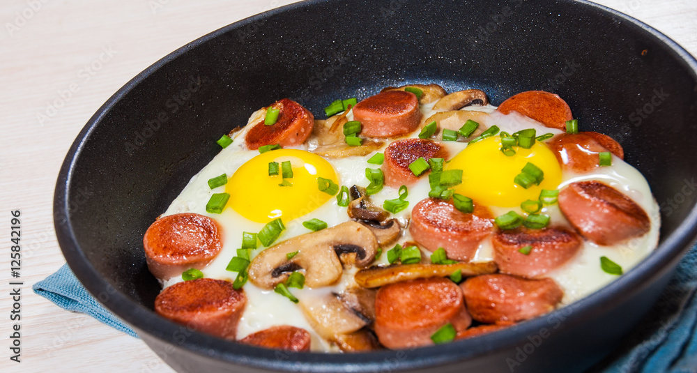 fried eggs with mushrooms and sausage in a frying pan