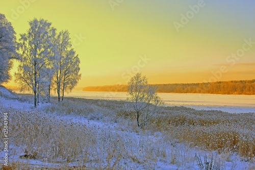 beautiful winter landscape at sunset with river and snow-covered trees