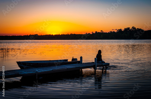 Tranquil silhouette of woman sitting on the dock on the shore of a calm lake in Minnesota