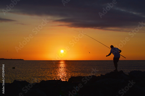 Silhouette of fisherman by the sea on sunrise 