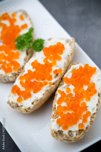 Red caviar on bread on white plate.