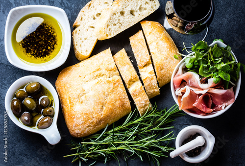 Ciabatta, pepper oil, jamon ham serrano, arugula, rosemary, slate background