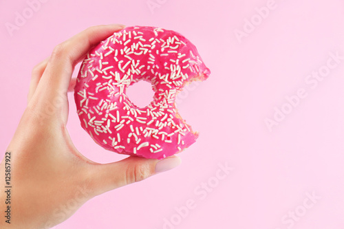 Female hand holding delicious donut on pink background, closeup