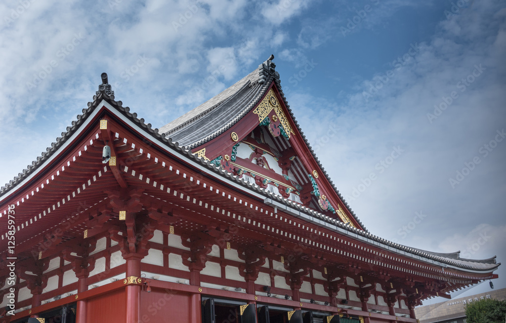 Tokyo, Japan - September 26, 2016: Part of the highly decorated vermilion roof of the Honzo main hall at Senso-ji Buddhist Temple under blue cloudy sky. Gold metalic decorations. Tokyo, Japan - September 26, 2016: Part of the highly decorated vermilion roof of the Honzo main hall at Senso-ji Buddhist Temple under blue cloudy sky. Gold metalic decorations.