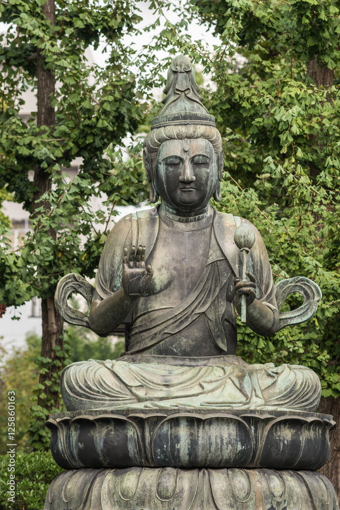 Tokyo, Japan - September 26, 2016: Closeup of bronze statue of Seishi Bosatsu, attendant of Amida Buddha, sitting on lotus pedestal in garden at Senso-ji Buddhist Temple. Green foliage. Tokyo, Japan - September 26, 2016: Closeup of bronze statue of Seishi Bosatsu, attendant of Amida Buddha, sitting on lotus pedestal in garden at Senso-ji Buddhist Temple. Green foliage.