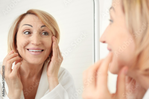 Senior woman doing facial anti aging massage near mirror
