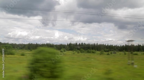 The view from the window of the train car. Summer day, clouds, green trees, power lines, railway crossing photo