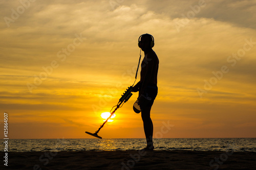 Treasure hunter with Metal detector on sunset the beach